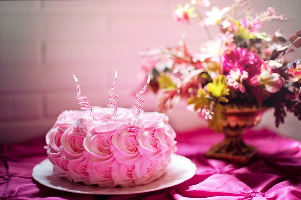 A beautifully decorated pink cake with curly candles and a floral bouquet, perfect for romantic celebrations.